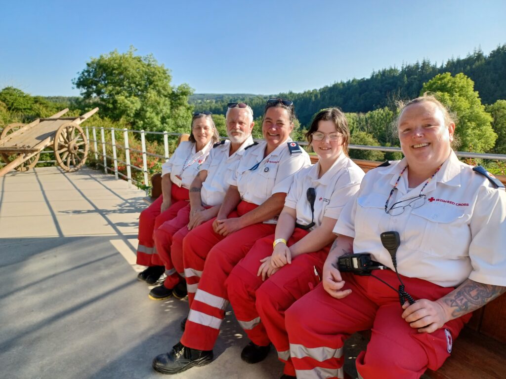 Five volunteers sitting down in front of a field, smiling for the camera