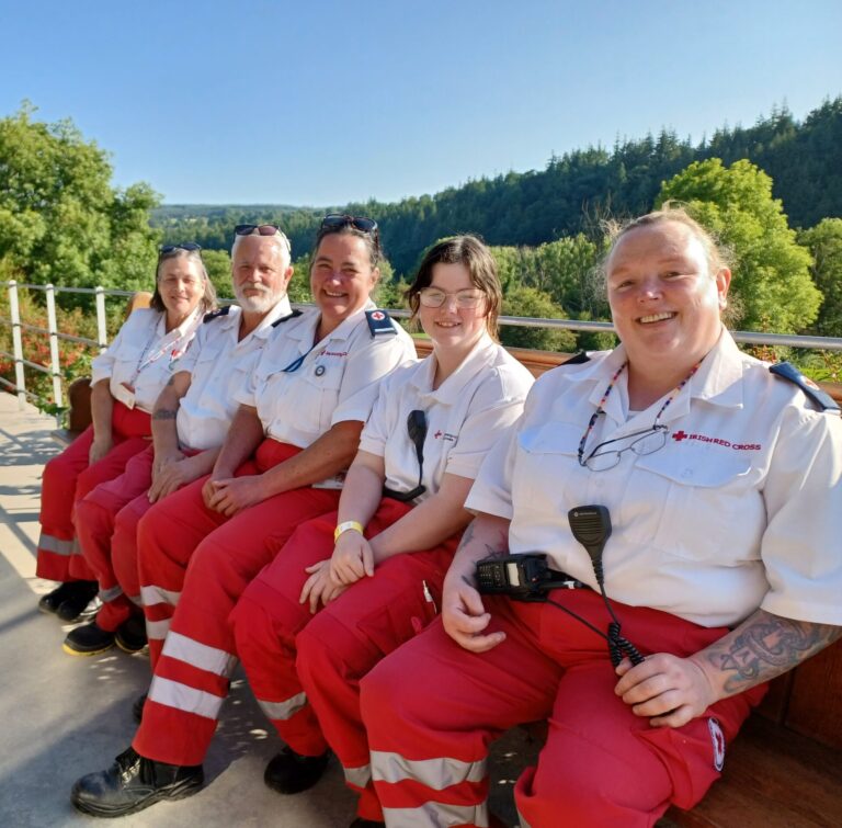 Five volunteers sitting down in front of a field, smiling for the camera