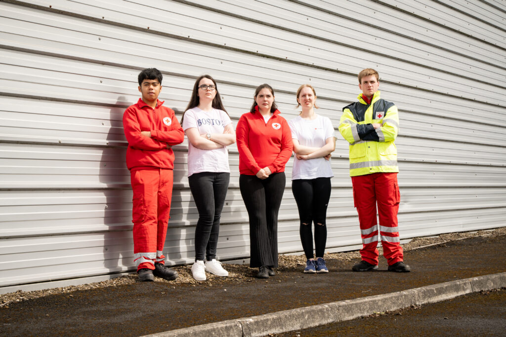 Five young adults posing with serious expressions and crossed arms.